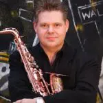 A man holding a saxophone in front of a wall.