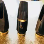 Three black and gold tenor saxophone mouthpieces on a table.