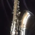 A silver saxophone is shown in the dark.