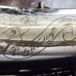 A silver saxophone with a design on it.