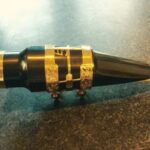 A black and gold SG Model Acrylic Jazz Tenor Mouthpiece on a table.